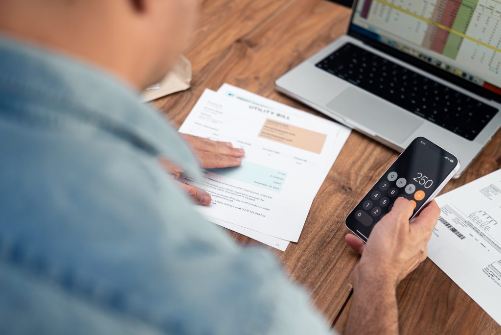 Person reviewing a utility bill with calculator and laptop